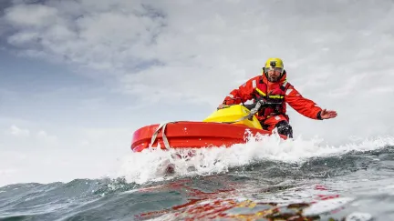 En frivillig sjöräddare sitter på en Rescuerunner och sträcker ut en hand.